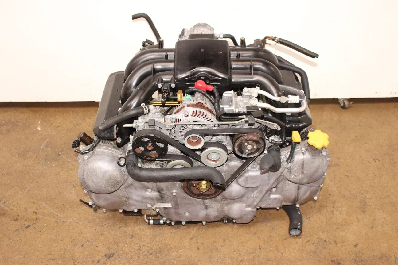 A Subaru Boxer car engine assembly viewed from the front, featuring a black intake manifold and metallic components.