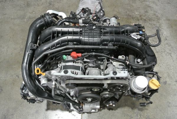 A Subaru FA/FB series boxer engine sitting on a concrete floor, showing the intake manifold, belt system, and accessories.