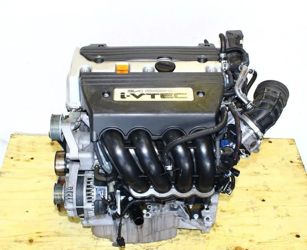 A Honda i-VTEC four-cylinder car engine on a wooden pallet against a white background.