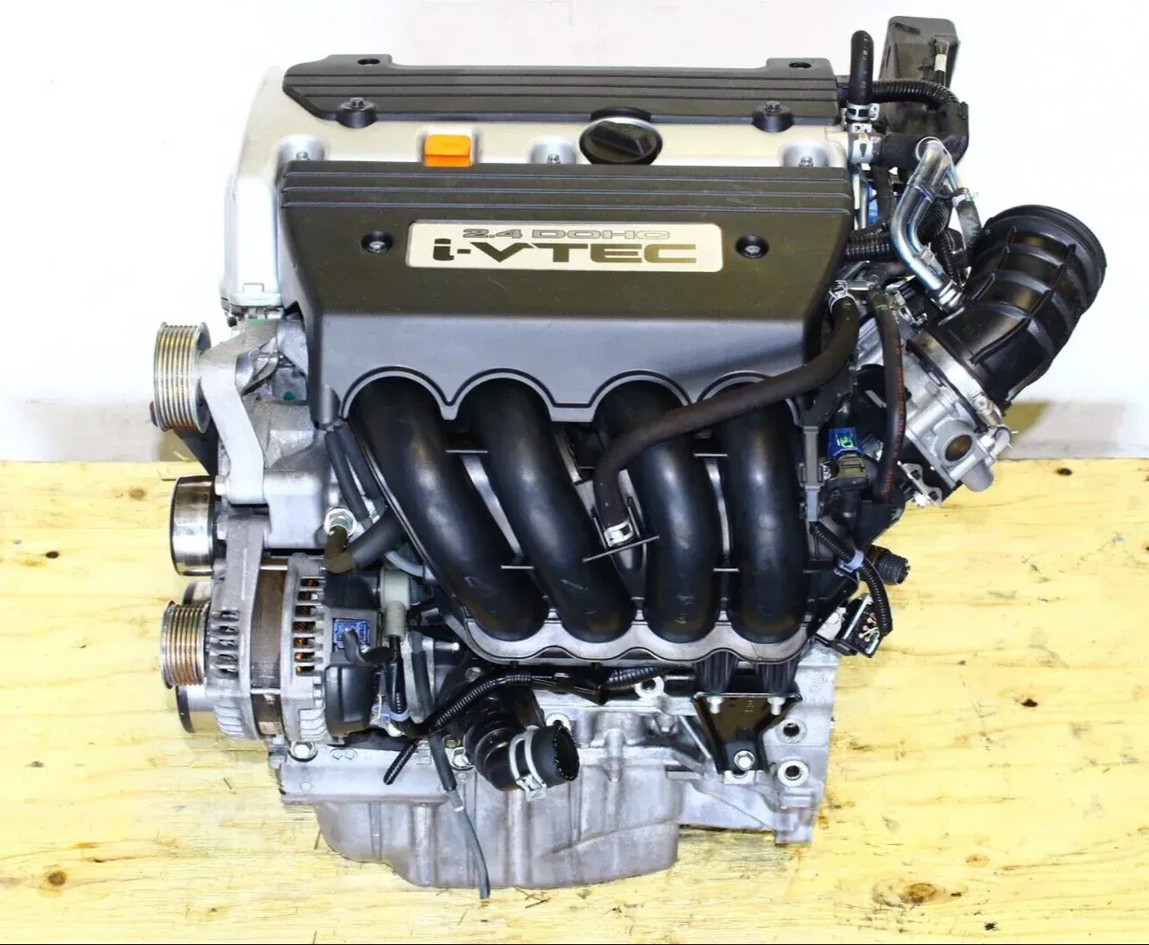 A silver and black Honda i-VTEC four-cylinder automotive engine sitting on a wooden surface.