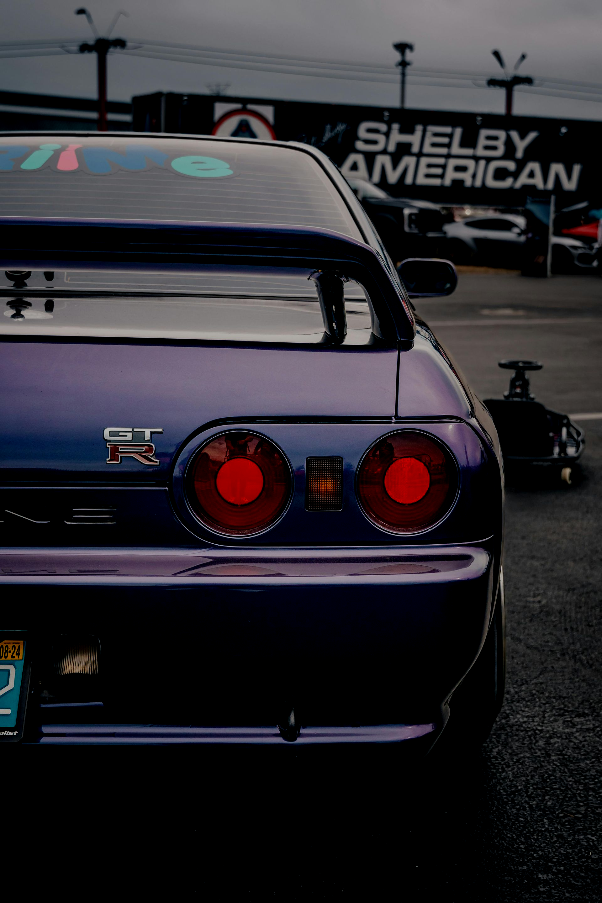 Rear view of a purple Nissan Skyline GT-R parked in front of a Shelby American building.