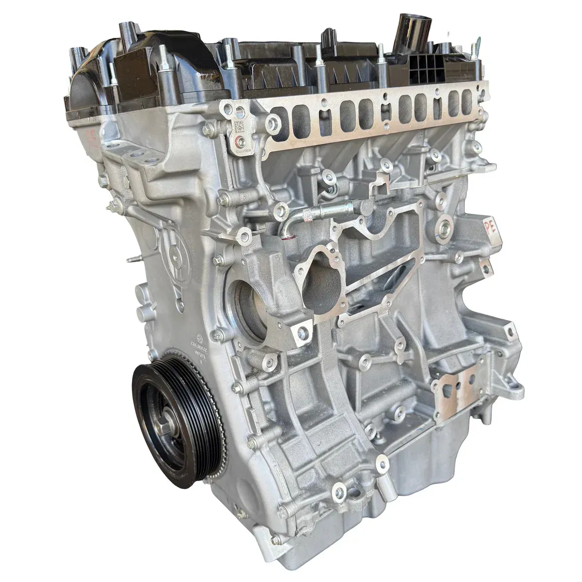 A silver-colored, four-cylinder automotive engine block assembly shown from a side angle, featuring a pulley wheel.