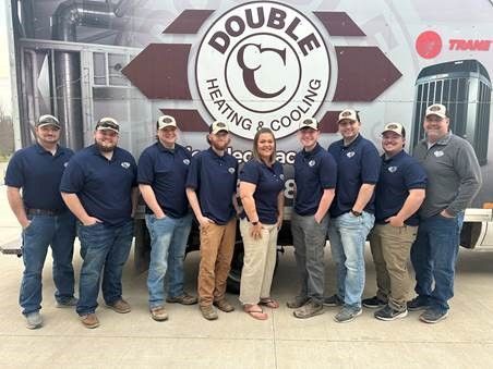 A group of people standing in front of a double c heating and cooling truck.