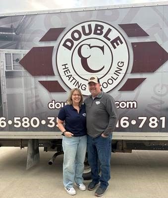 A man and a woman are standing in front of a double c heating and cooling truck.