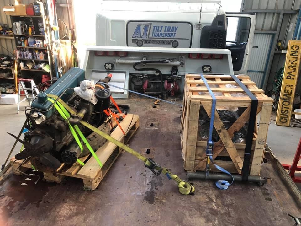 A motor is sitting on a wooden pallet in front of a truck.