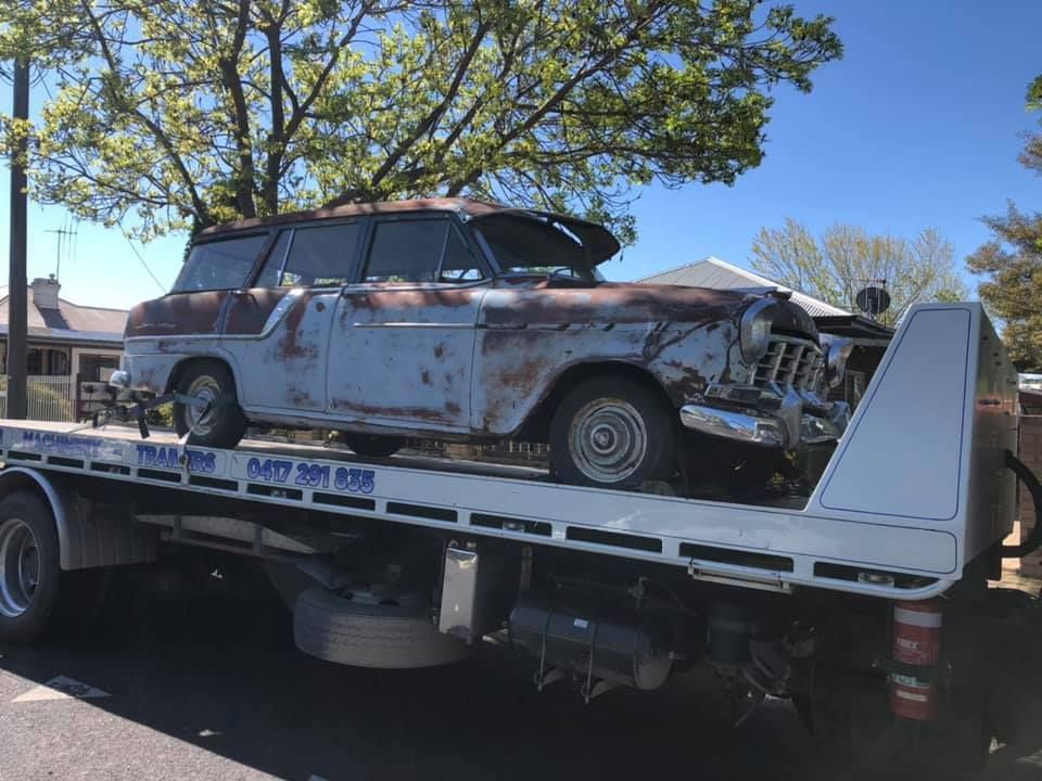 An old rusty car is sitting on top of a tow truck.