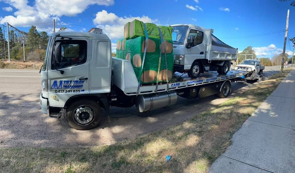 A tow truck with a dump truck on the back is parked on the side of the road.