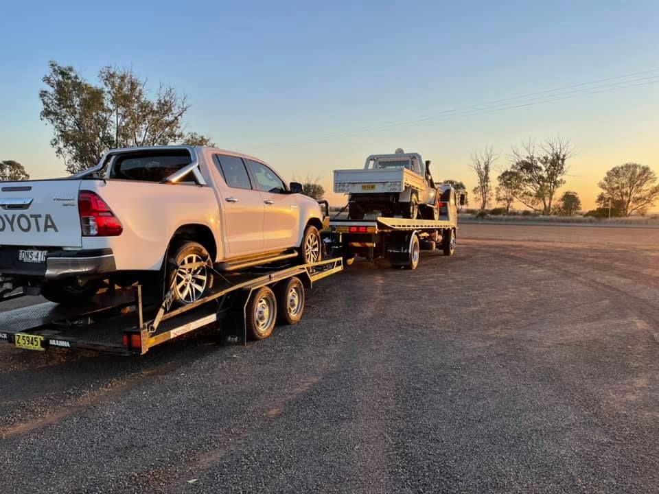 A white toyota truck is being towed by a trailer.