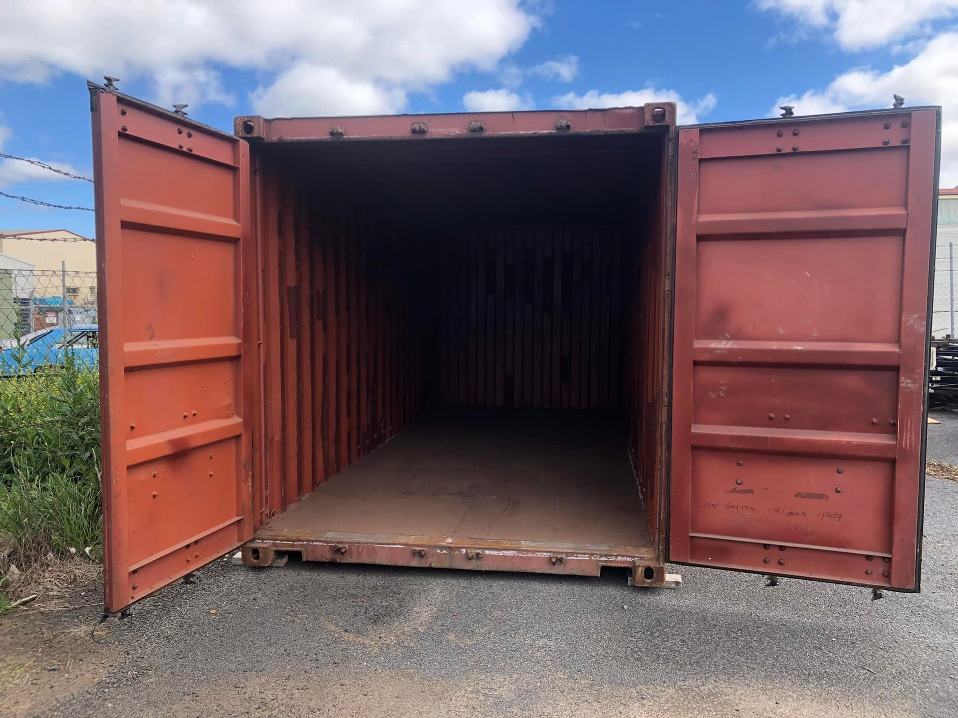 An empty shipping container with its doors open on a gravel road.