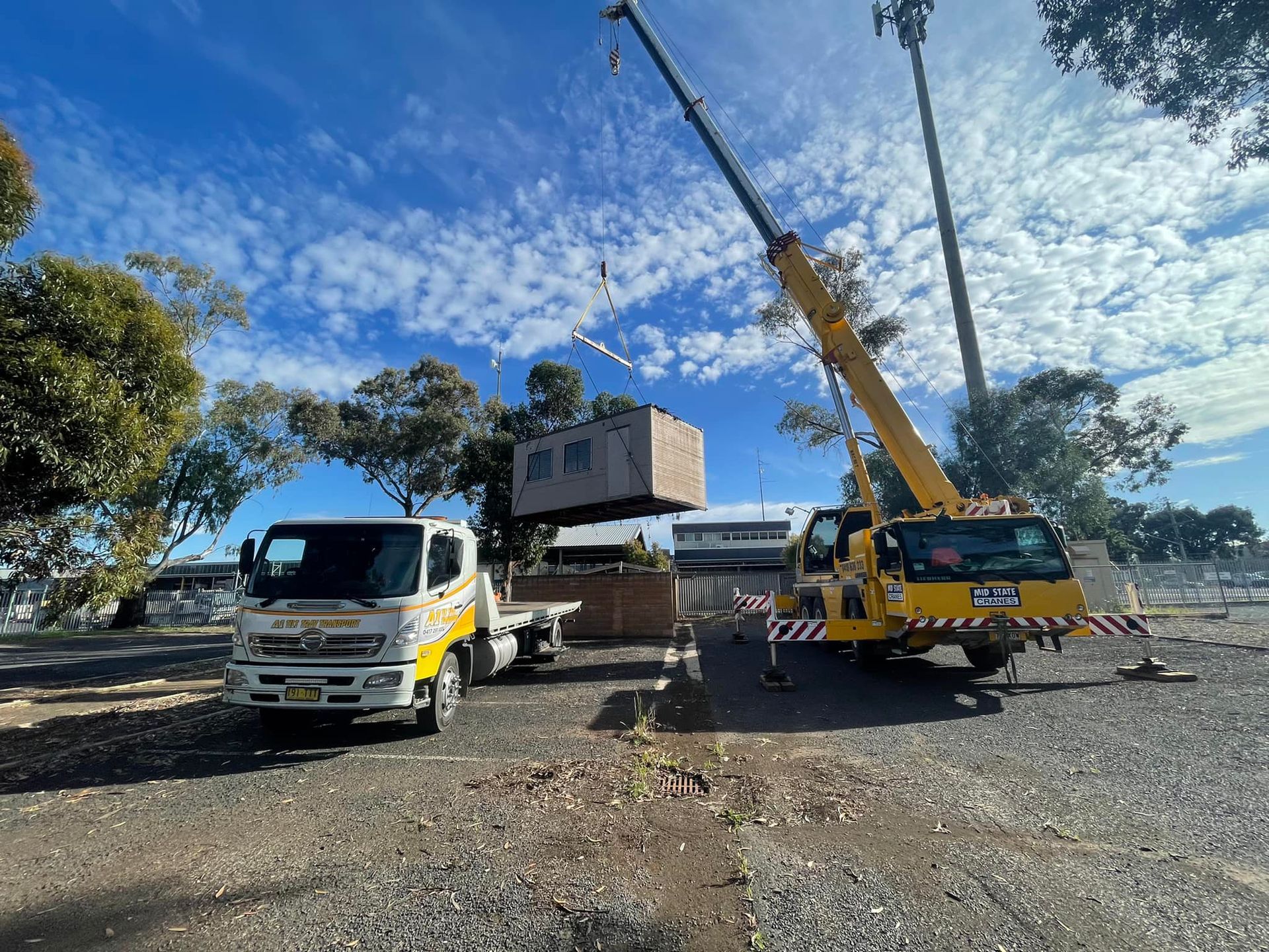 A truck is being lifted by a crane in a gravel lot.