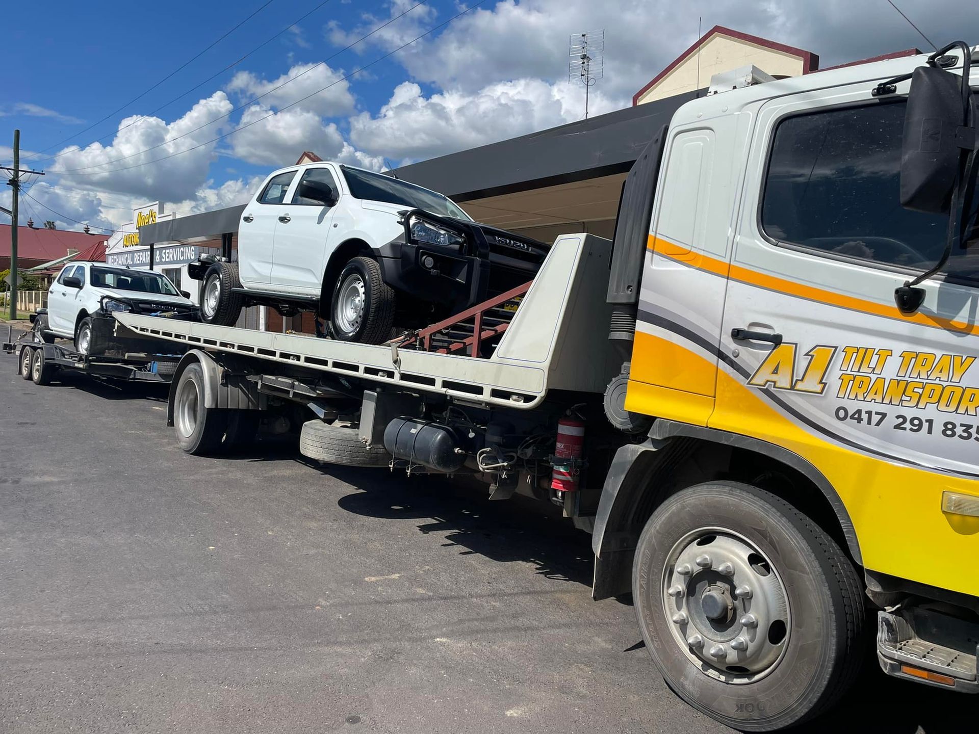 A tow truck is carrying two cars on a trailer.