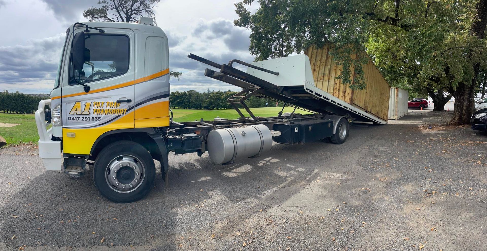 A tow truck with a container on the back is parked in a gravel lot.