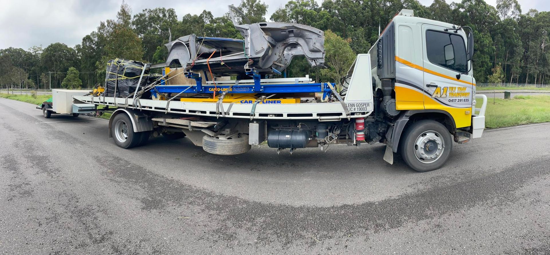 A tow truck is carrying a trailer full of junk on a road.