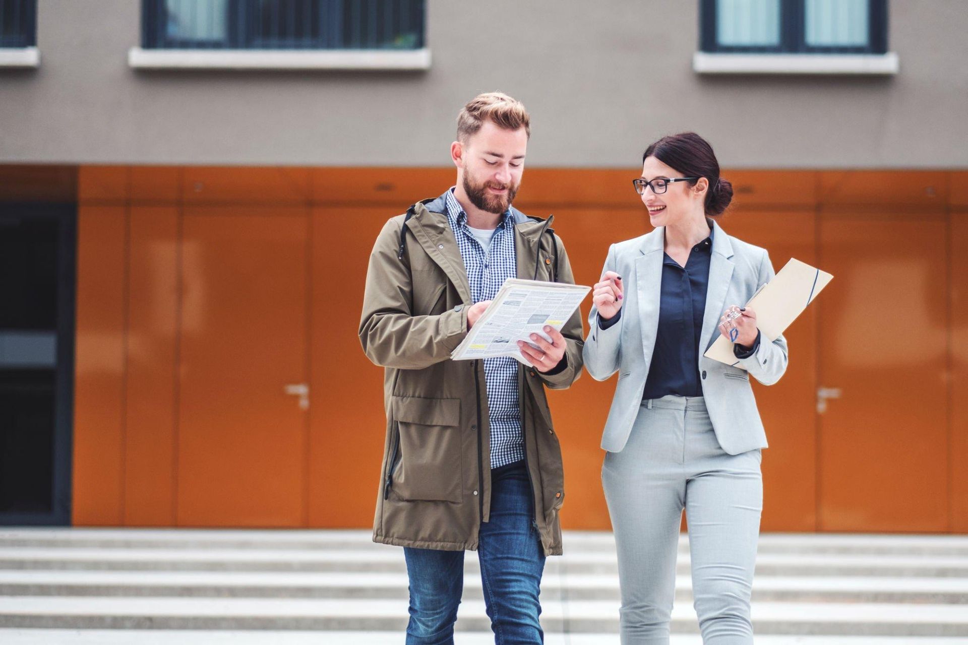 A man and a woman are standing in front of a building looking at a piece of paper.