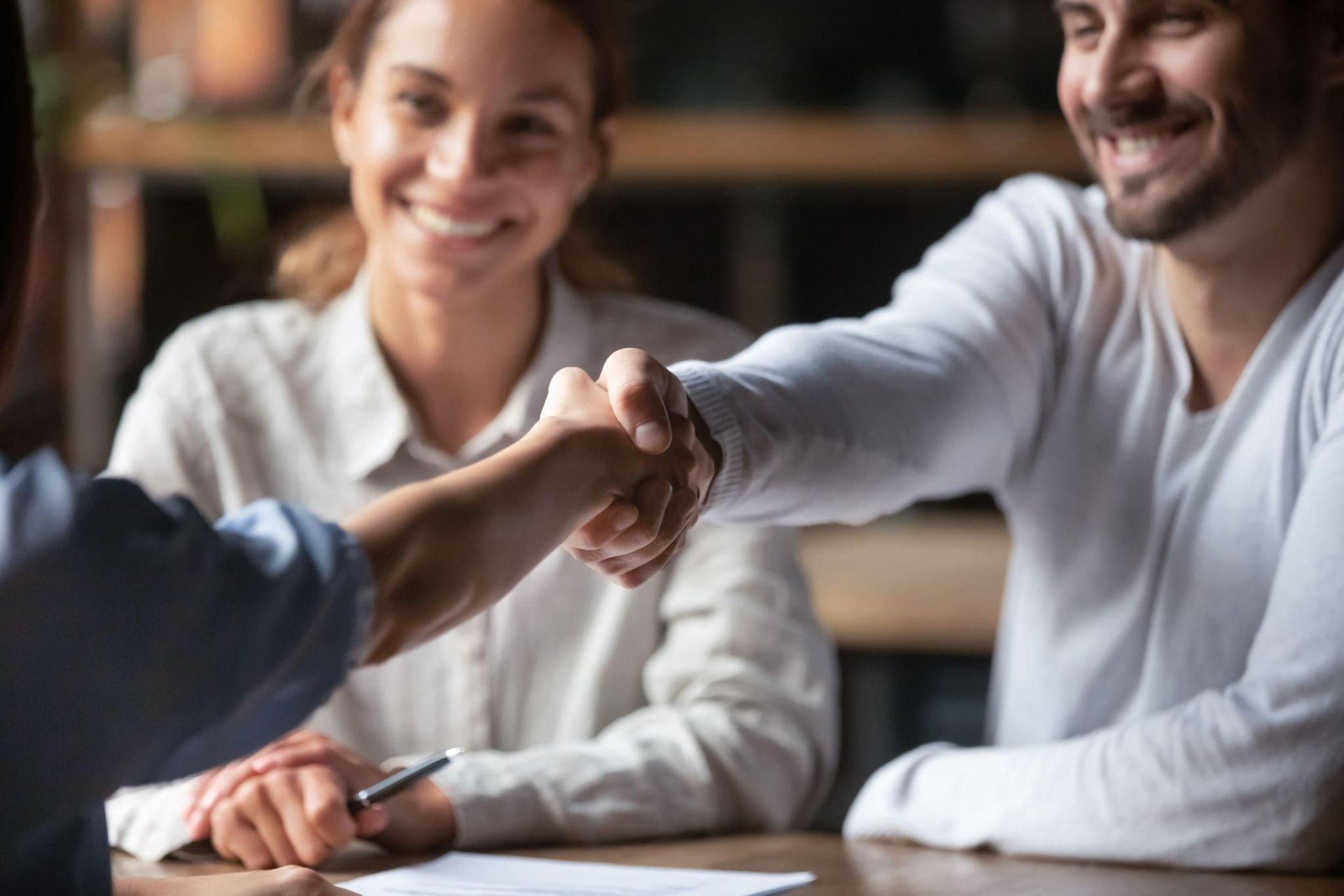 A man and a woman are shaking hands while sitting at a table.