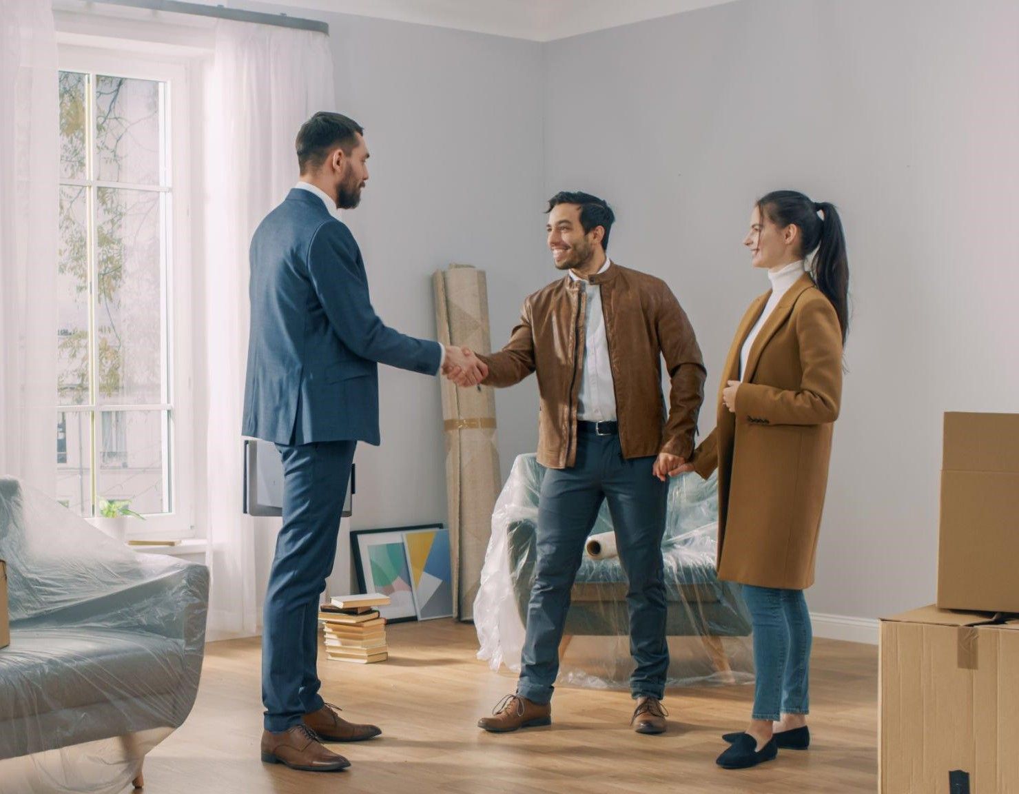 A man and woman are shaking hands with a real estate agent in a living room.