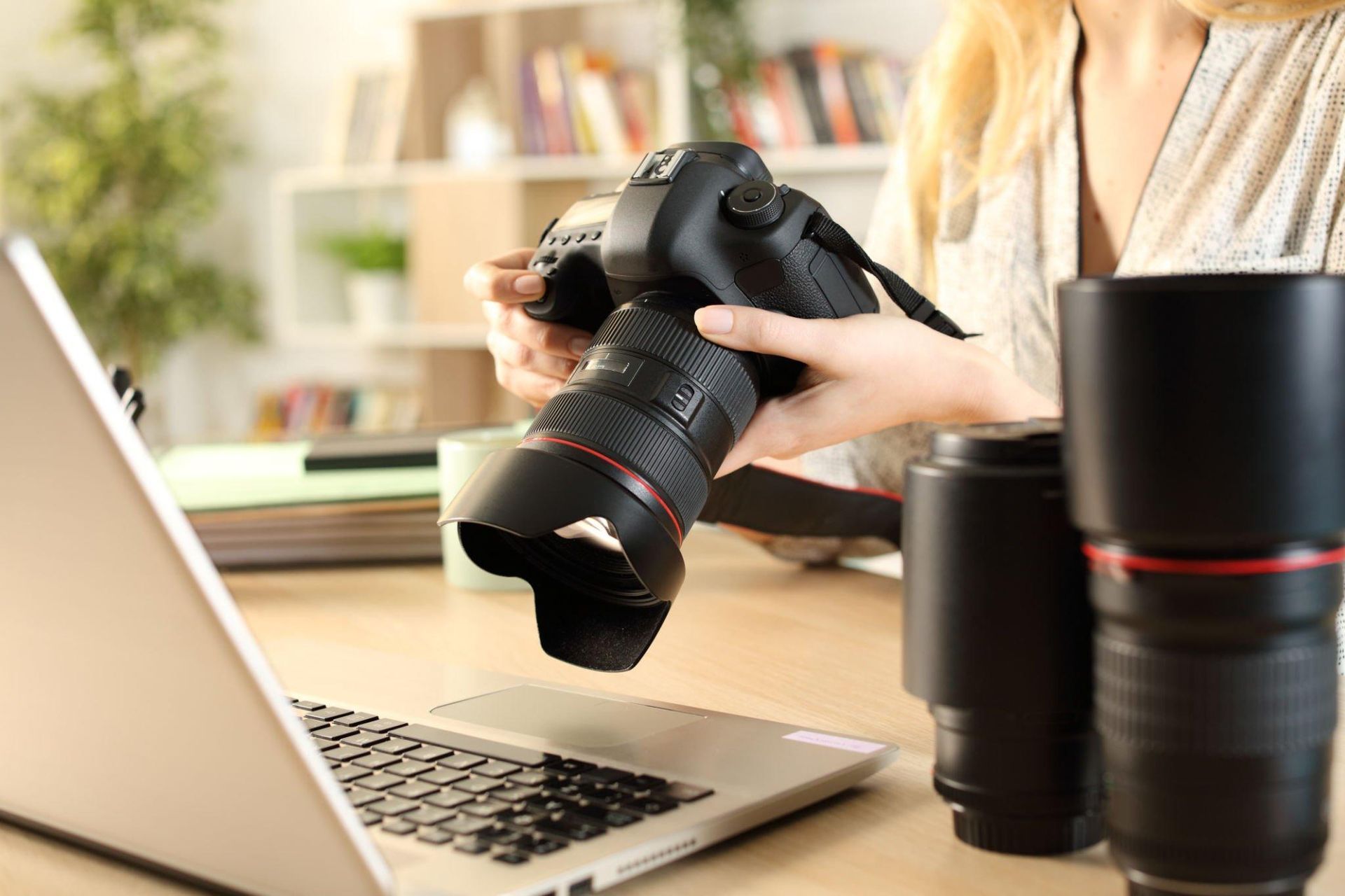 A woman is holding a camera in front of a laptop computer.