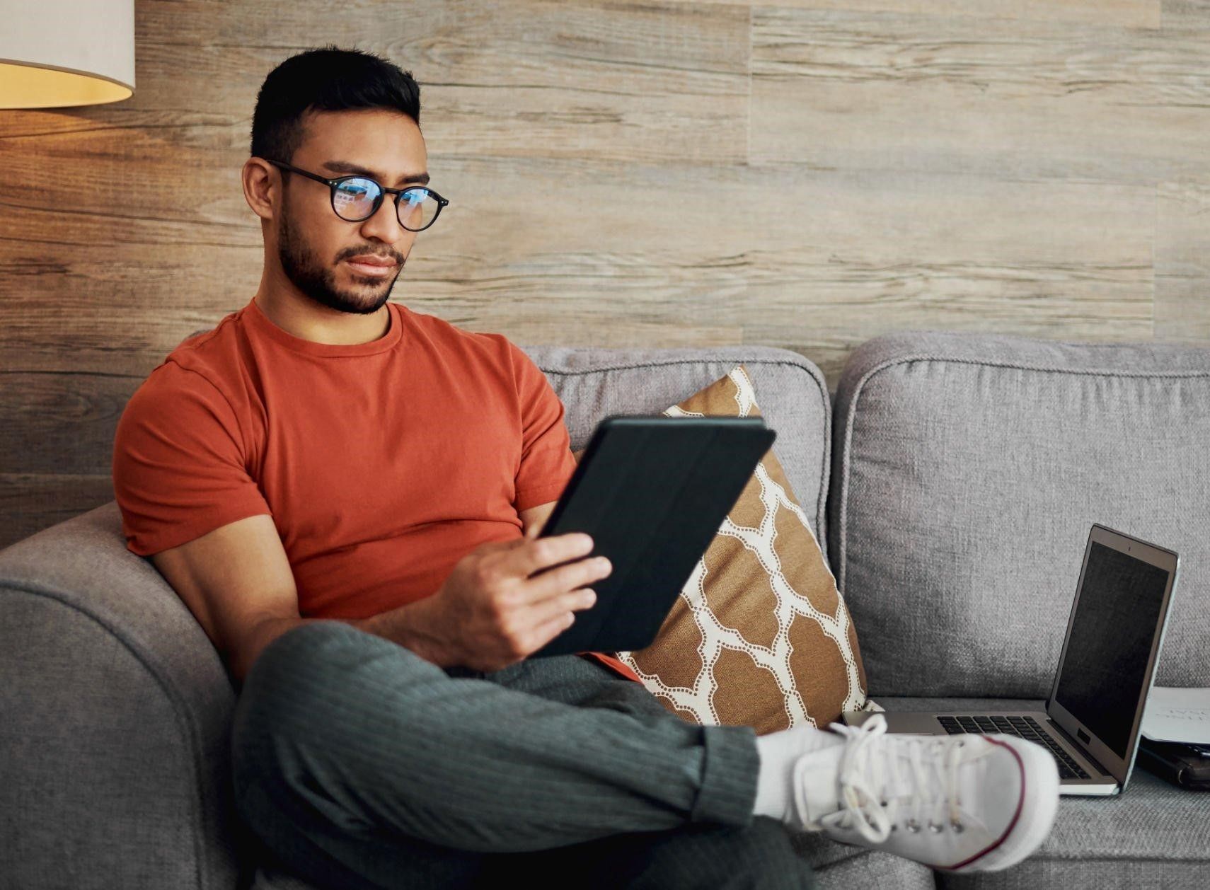 A man is sitting on a couch using a tablet computer.