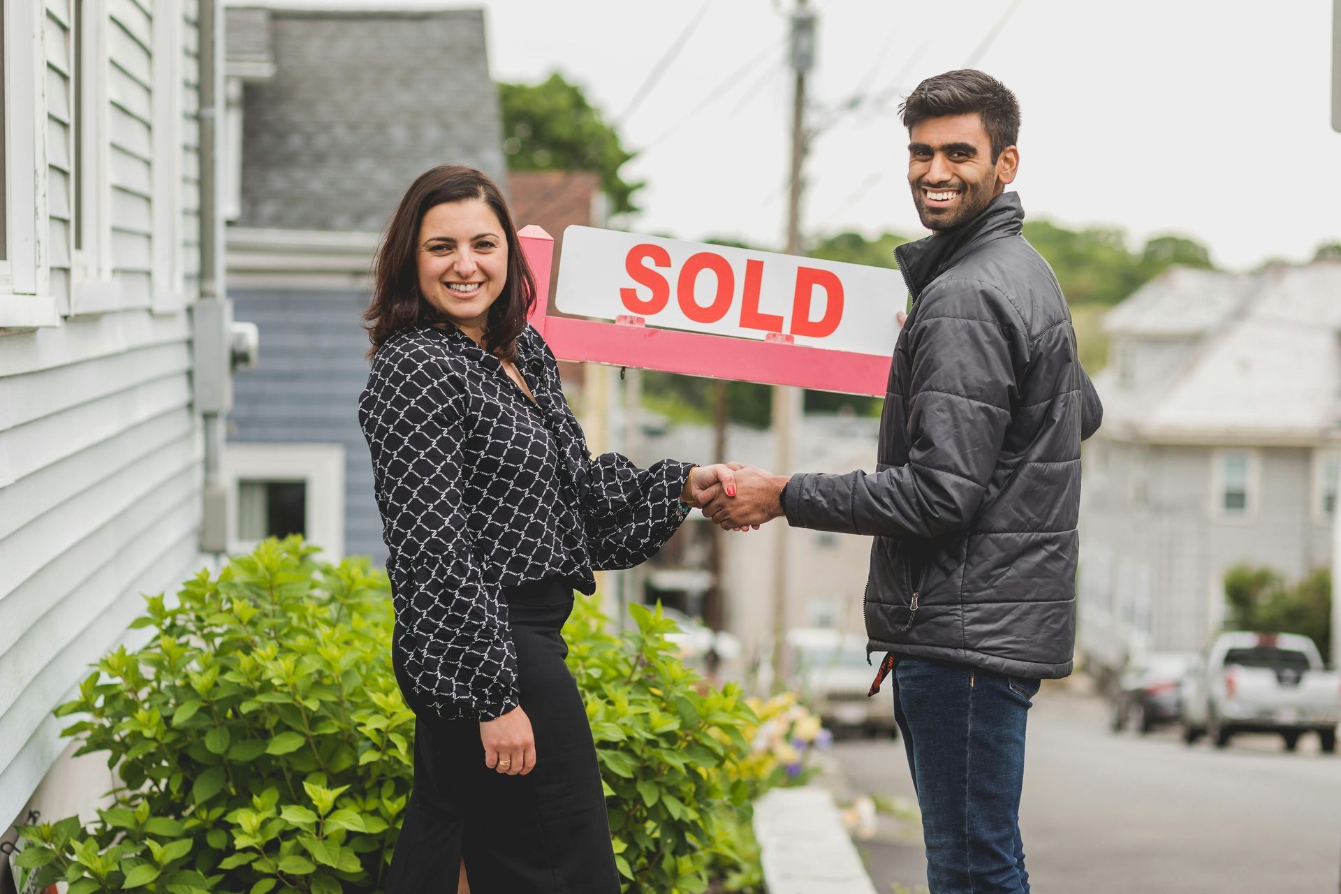 A man and a woman are shaking hands in front of a sold sign.
