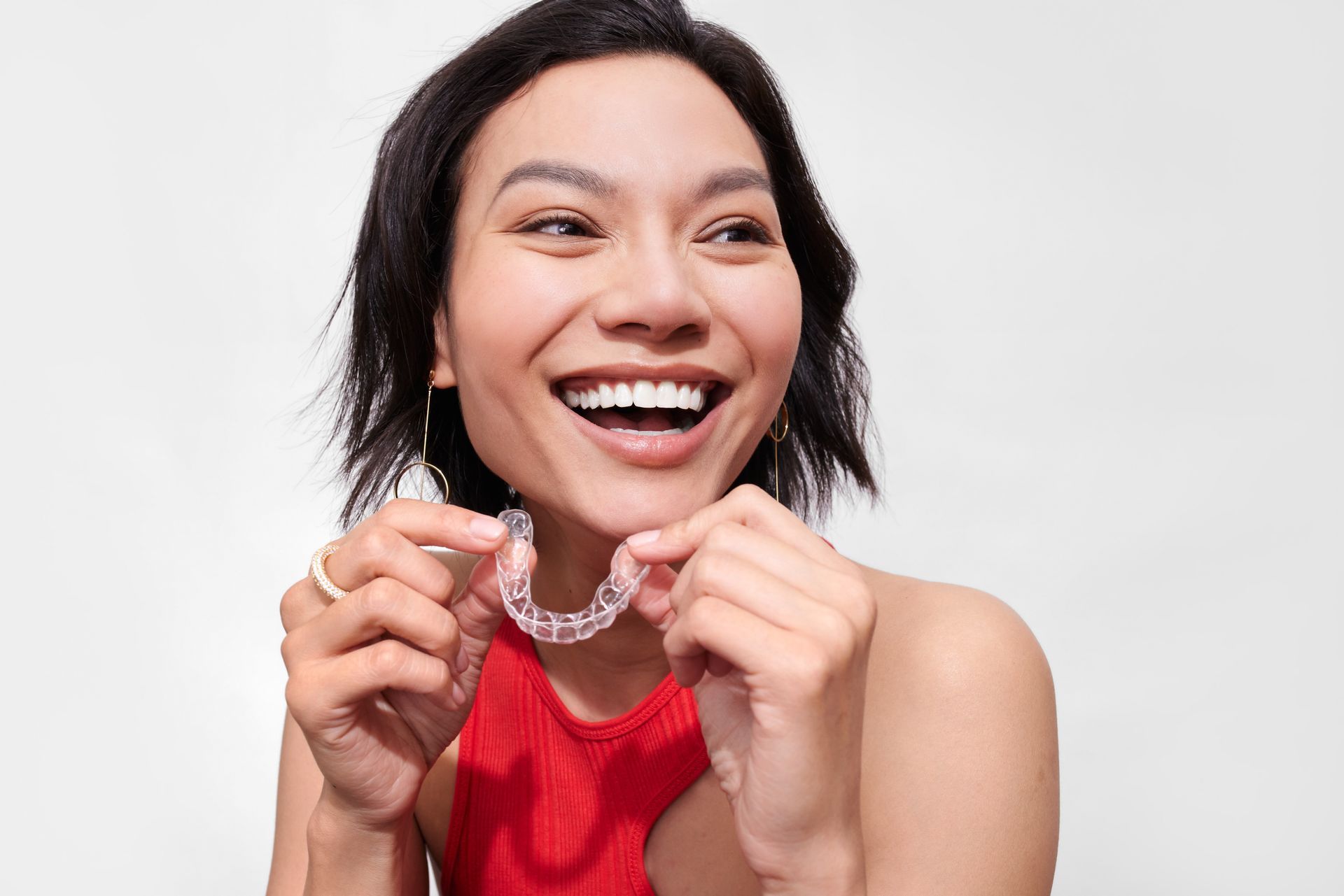 A woman is holding a clear retainer in her hands and smiling.