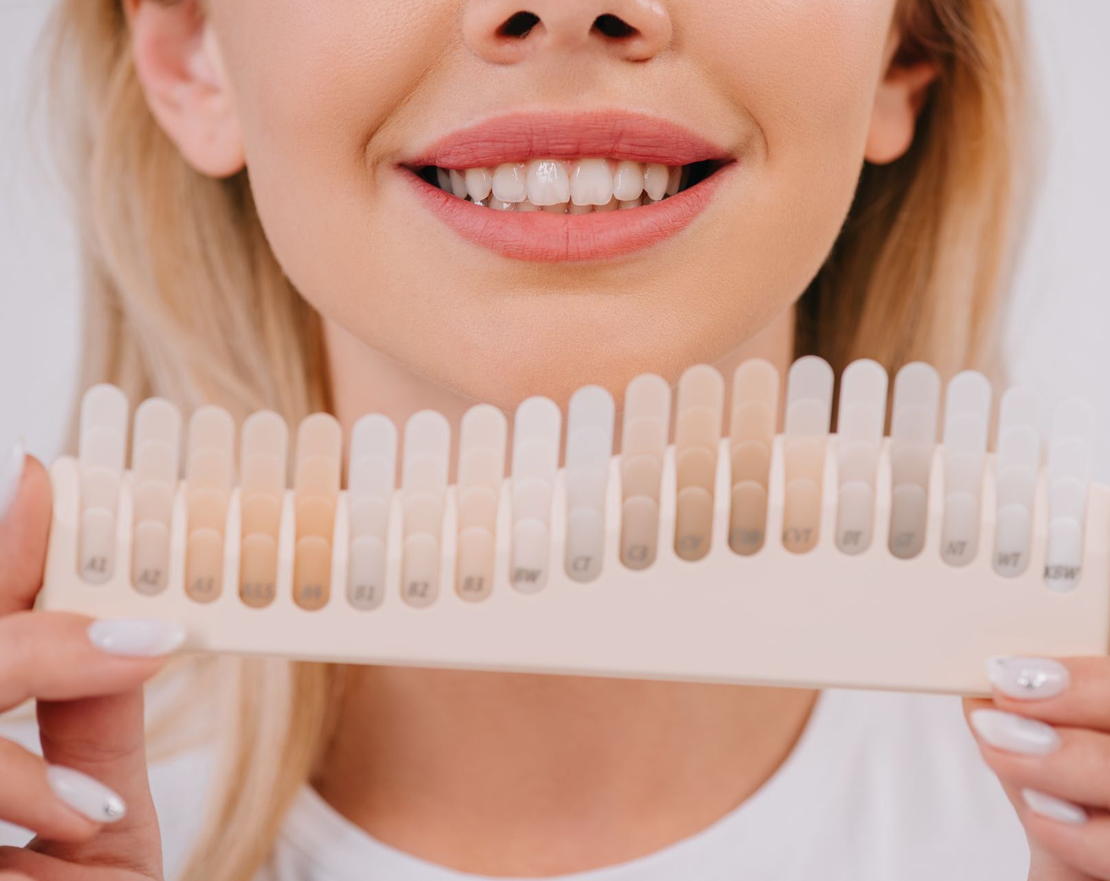 A woman is holding a tooth color chart in front of her mouth.