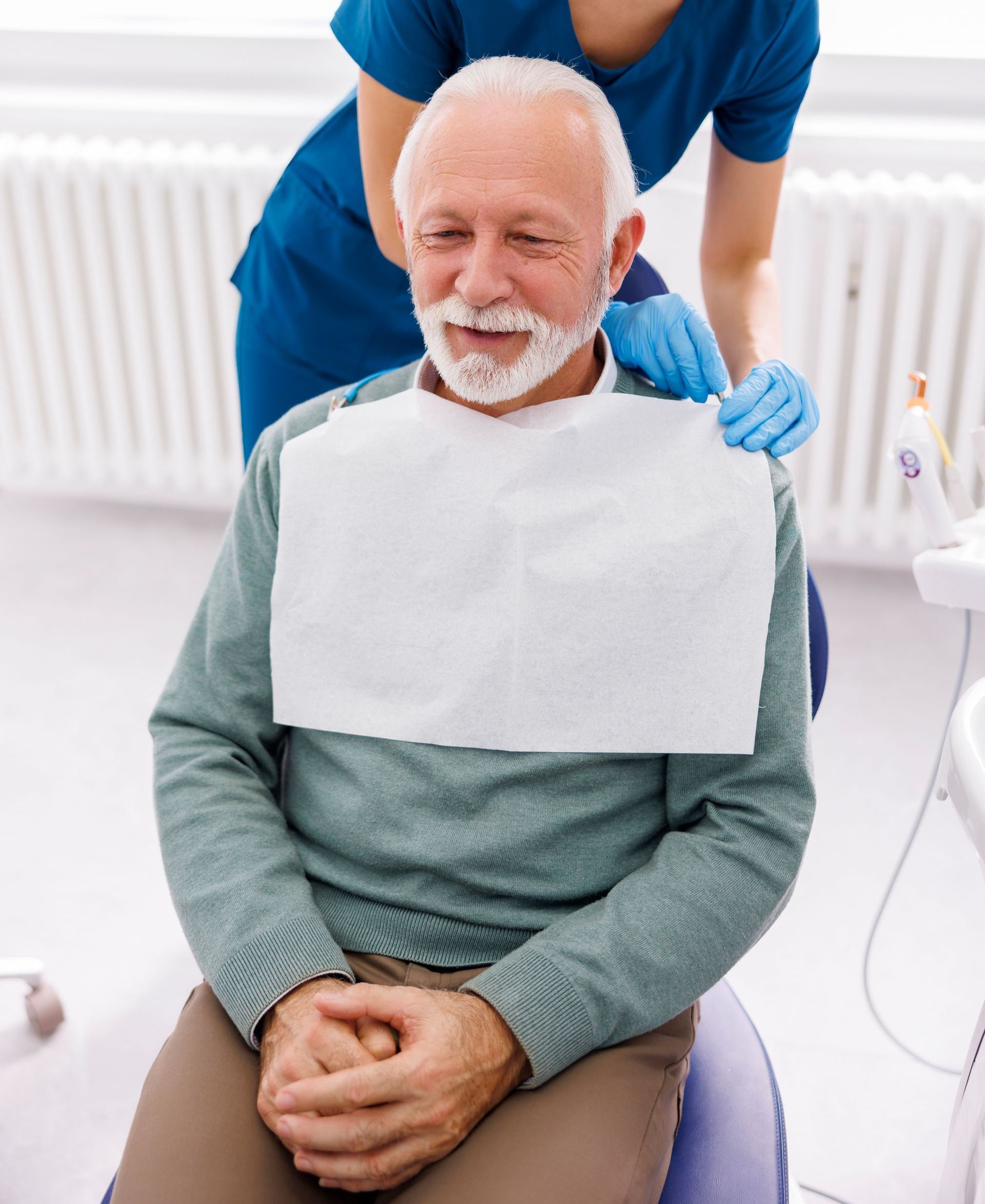 A man with a beard is sitting in a dental chair with a napkin around his neck.