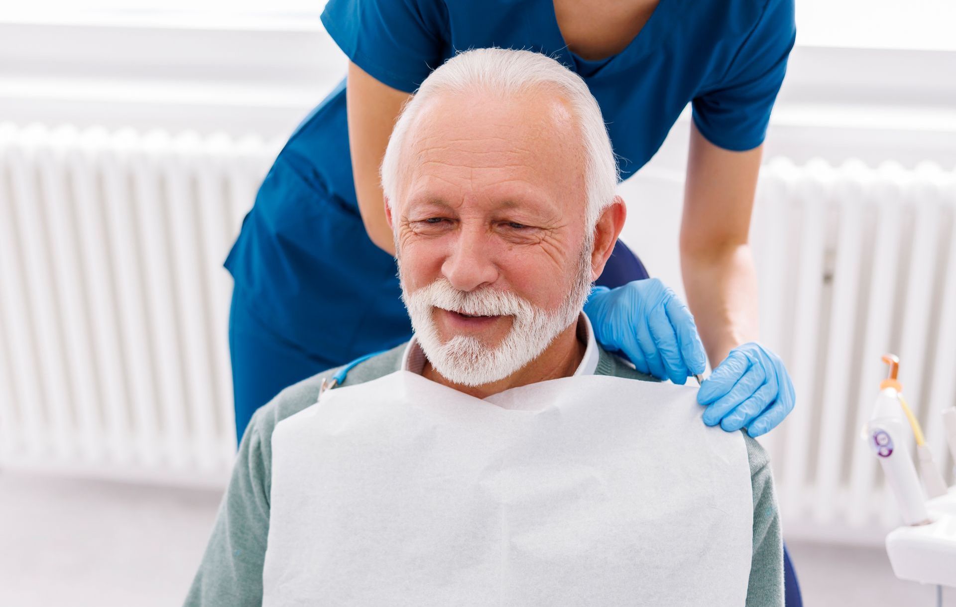 An elderly man is smiling while sitting in a dental chair.