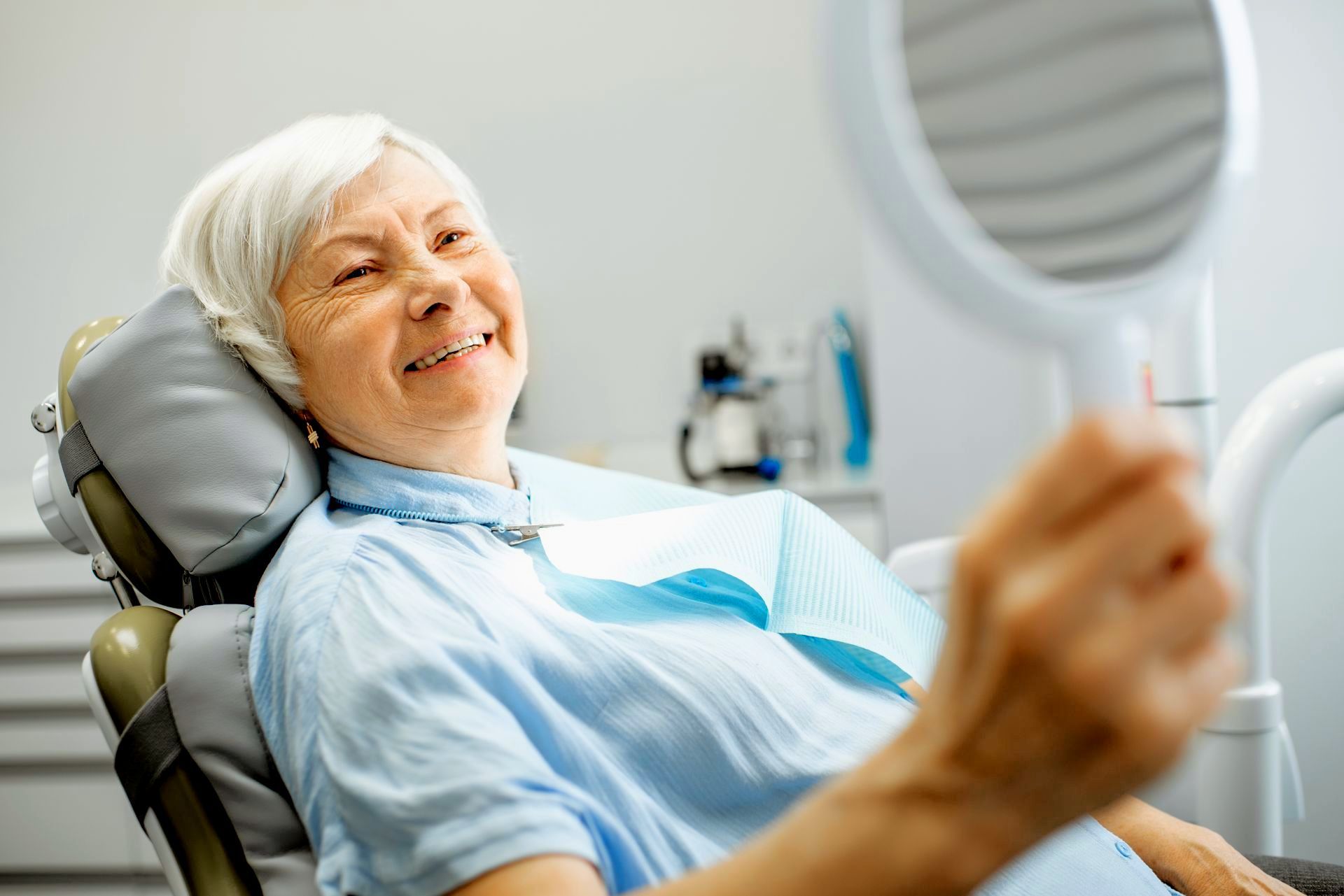 woman smiling in mirror at dental office getting dental implant dentures | Hunt Valley MD