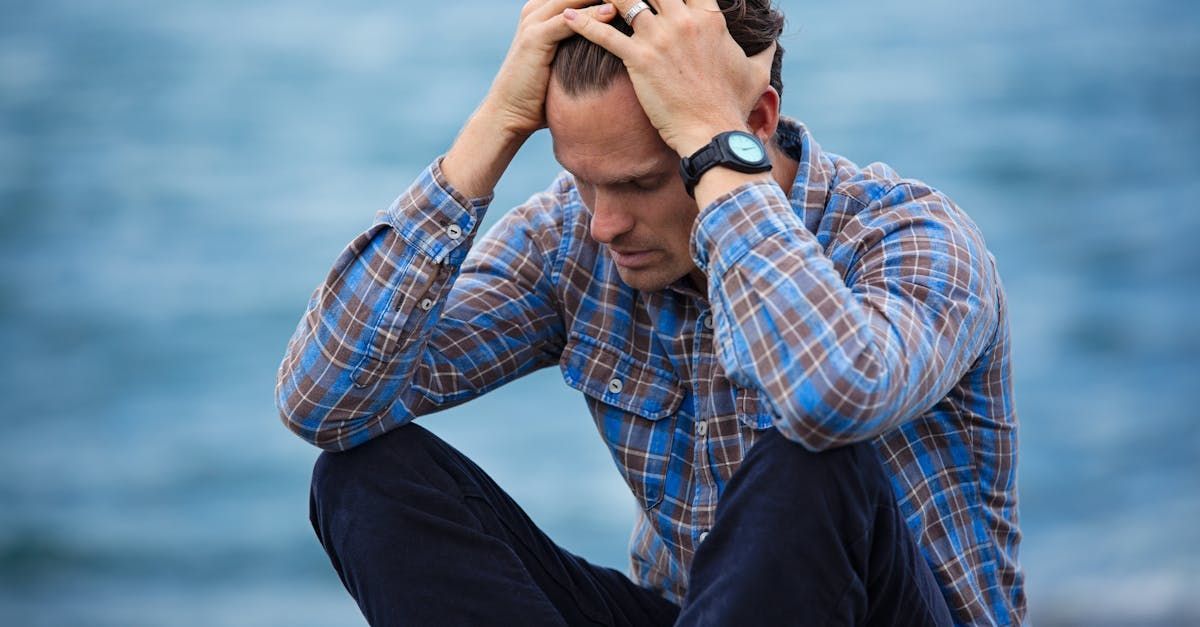 A man is sitting on the beach with his hands on his head.