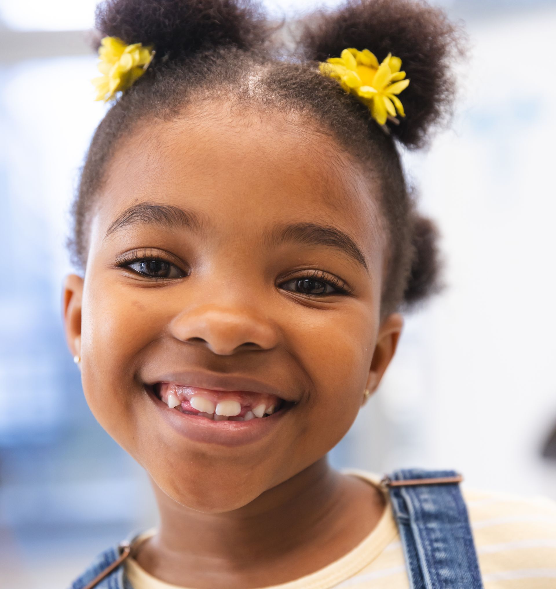 A little girl with two yellow flowers in her hair is smiling