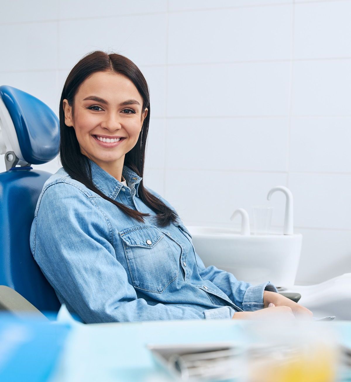 A woman is sitting in a dental chair and smiling.