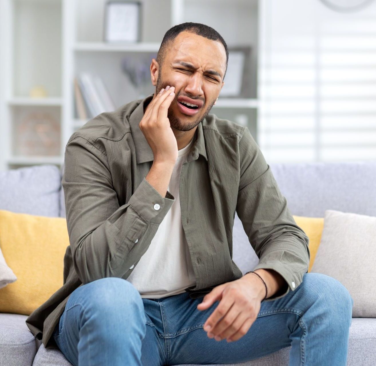 A man is sitting on a couch with a toothache.