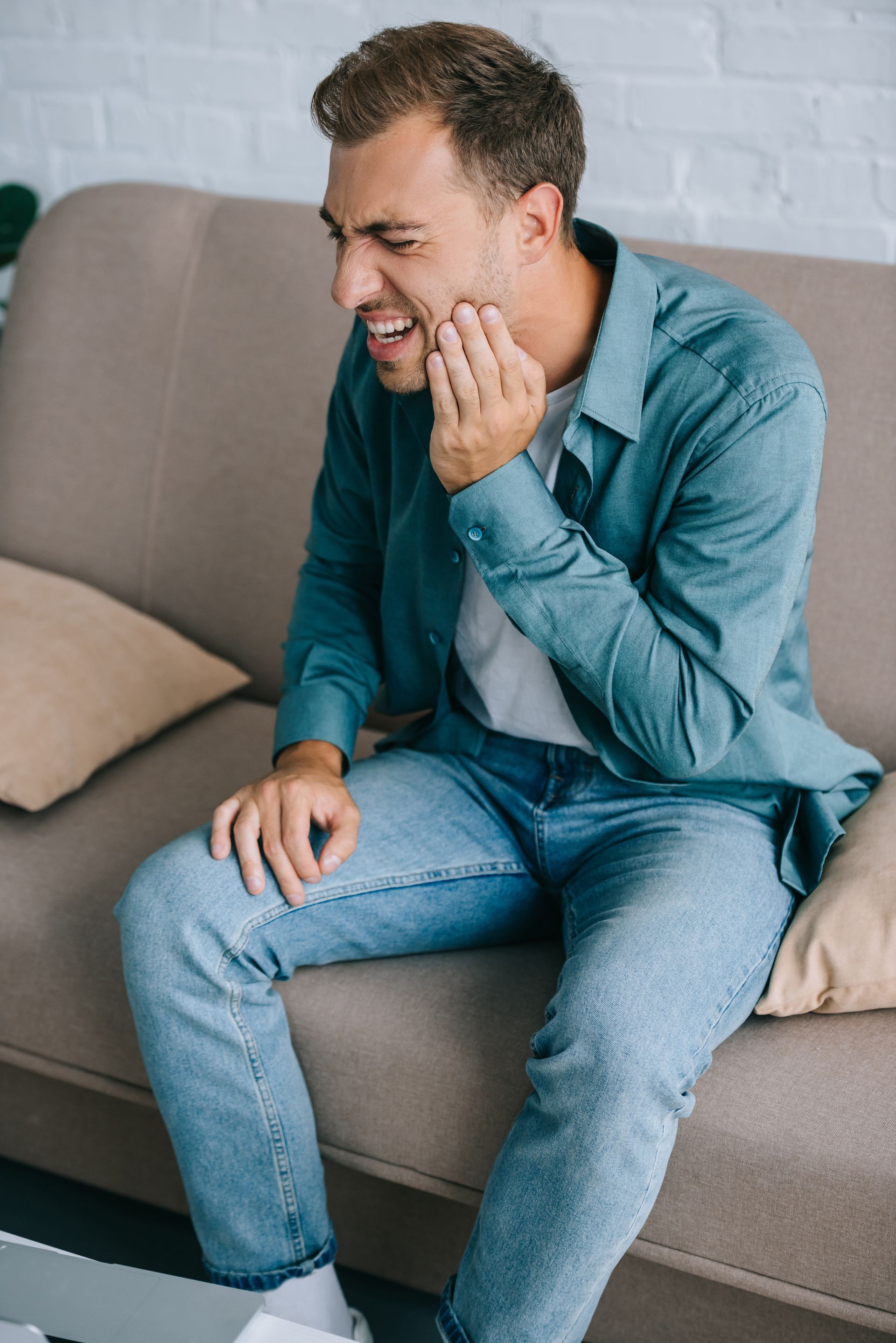 A man is sitting on a couch with a toothache.