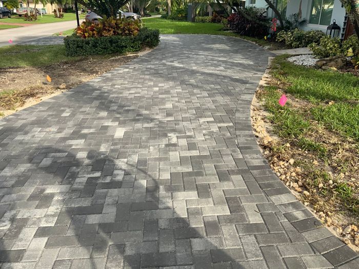 Two men are working on a gravel driveway in front of a house.