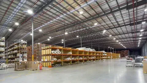Large warehouse interior with rows of shelves filled with goods, and bright overhead lighting.