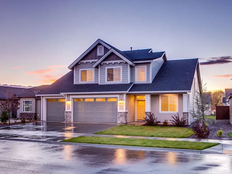 Two-story house with a gray exterior, two-car garage, and lush green lawn reflecting the twilight sky after rain.