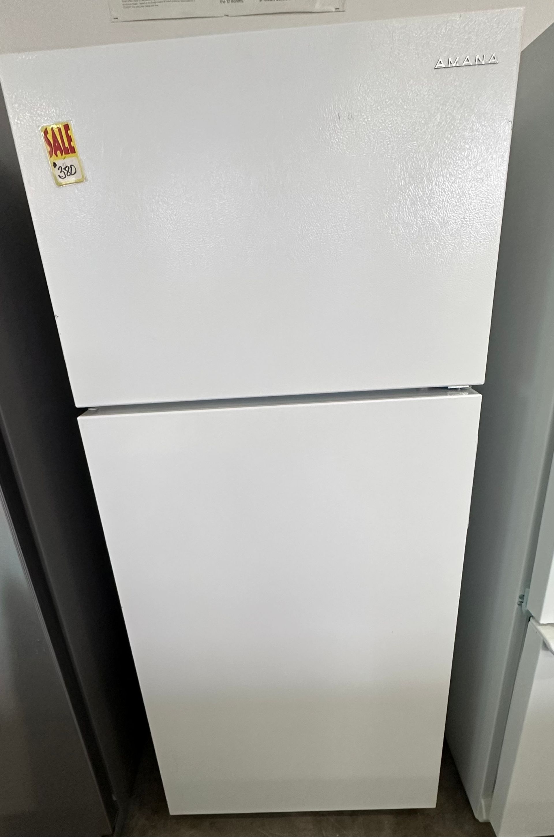 White top-freezer refrigerator in a room, with a sale sticker on the door.