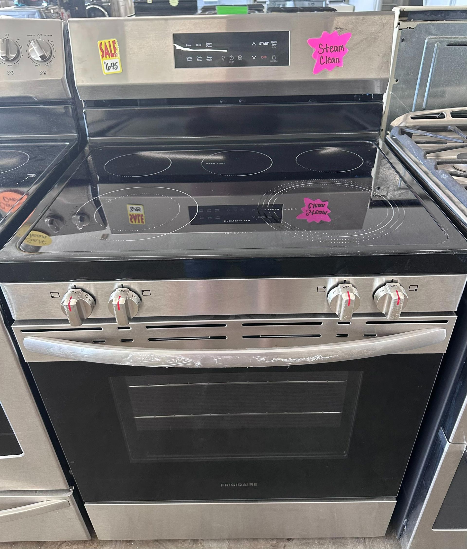 Stainless steel electric range with black glass cooktop and oven, knobs, price tag.