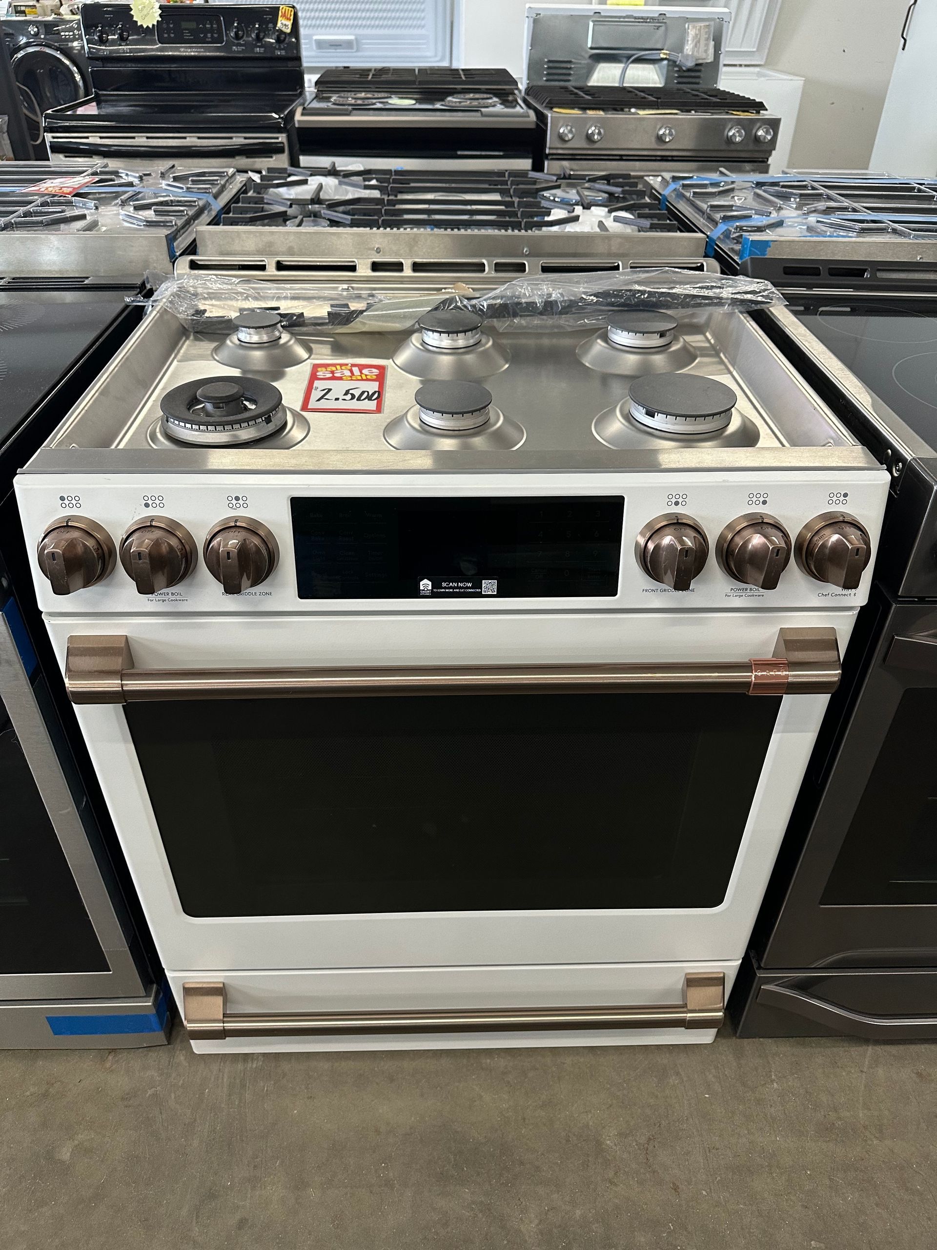 White and copper range with four burners, oven. Several other ranges visible in the background.