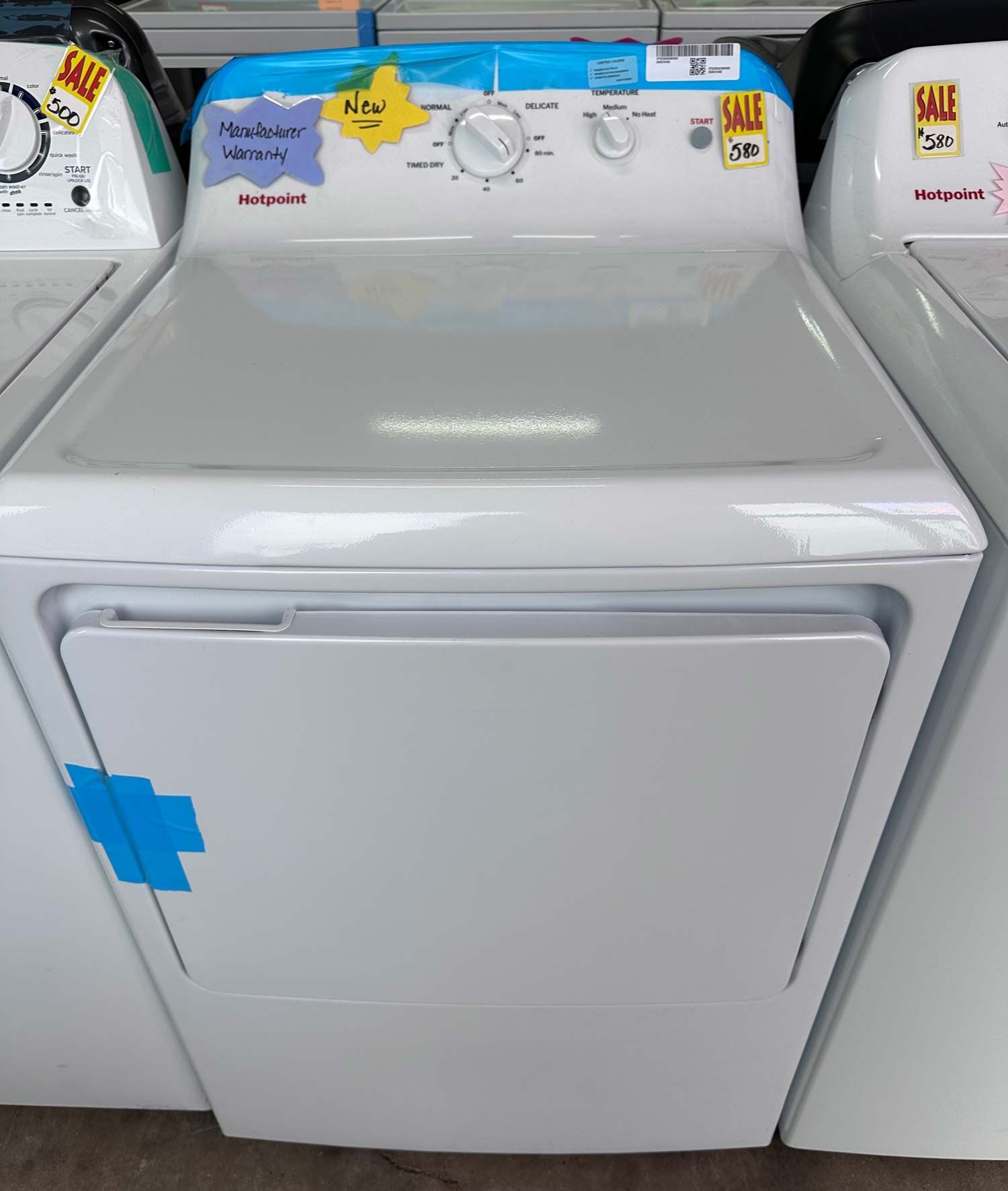 A white Hotpoint electric clothes dryer with a top-mounted control panel on display in a retail store.