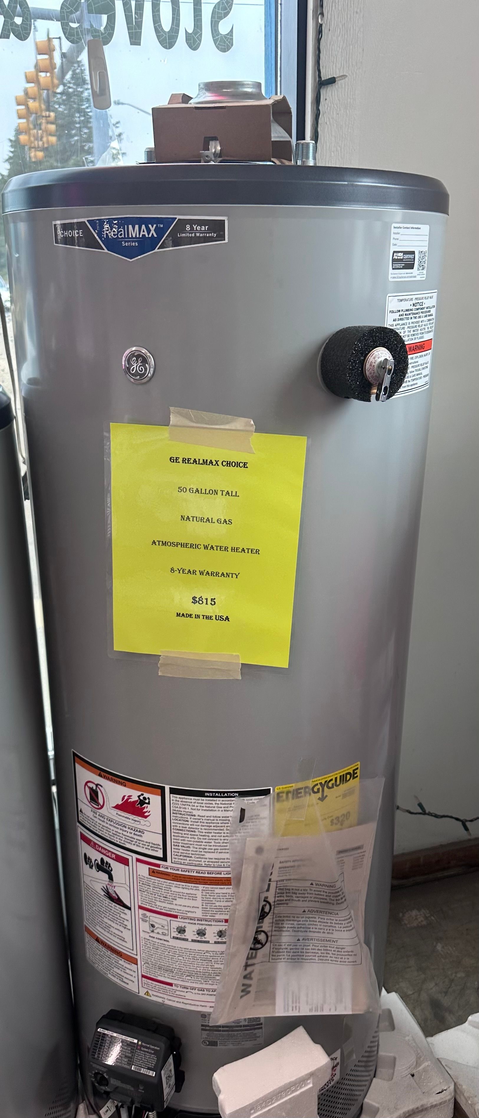 A silver water heater with a yellow sign taped to it.