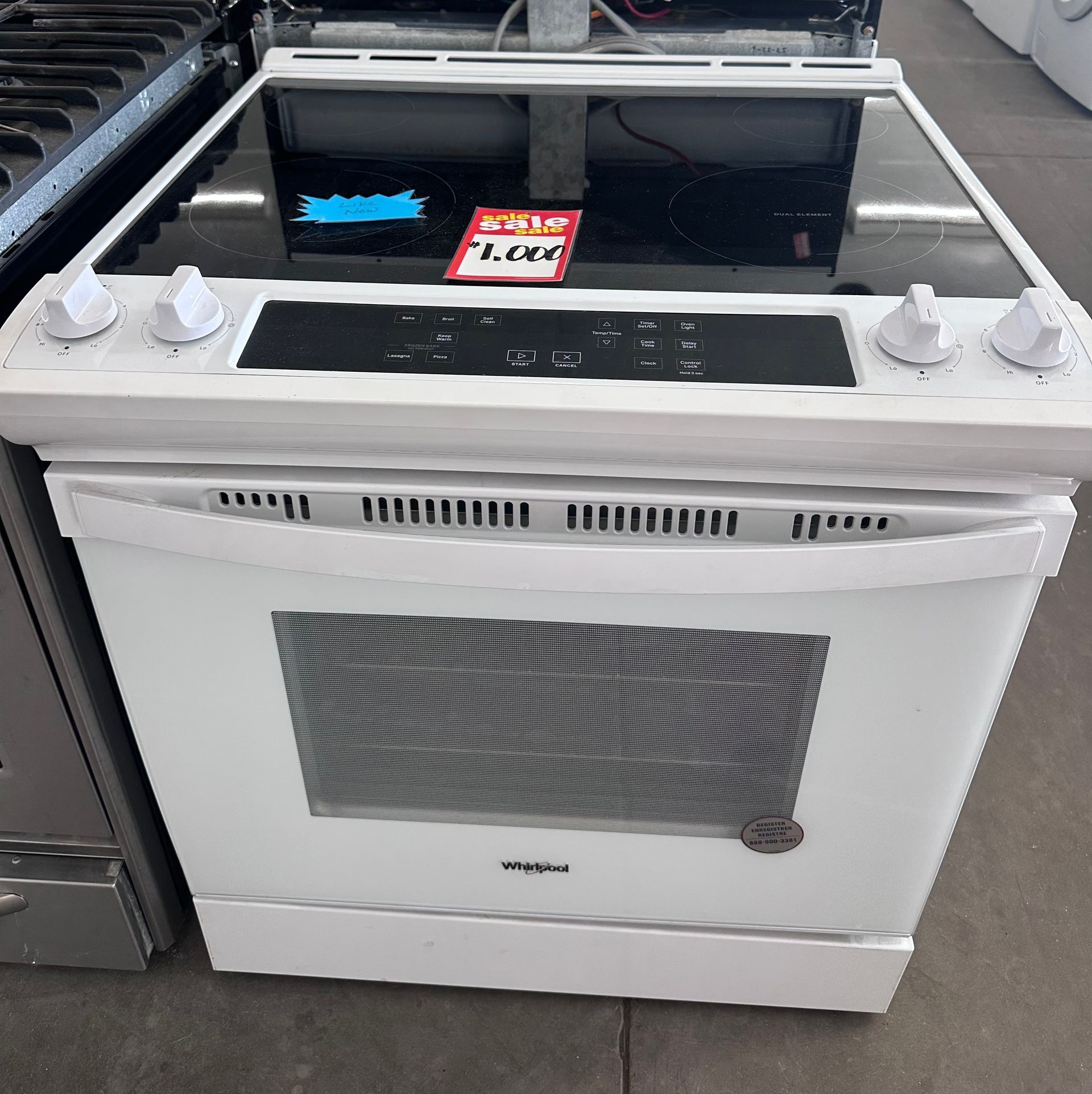 White Whirlpool electric range with a glass cooktop and oven, displayed in a store.