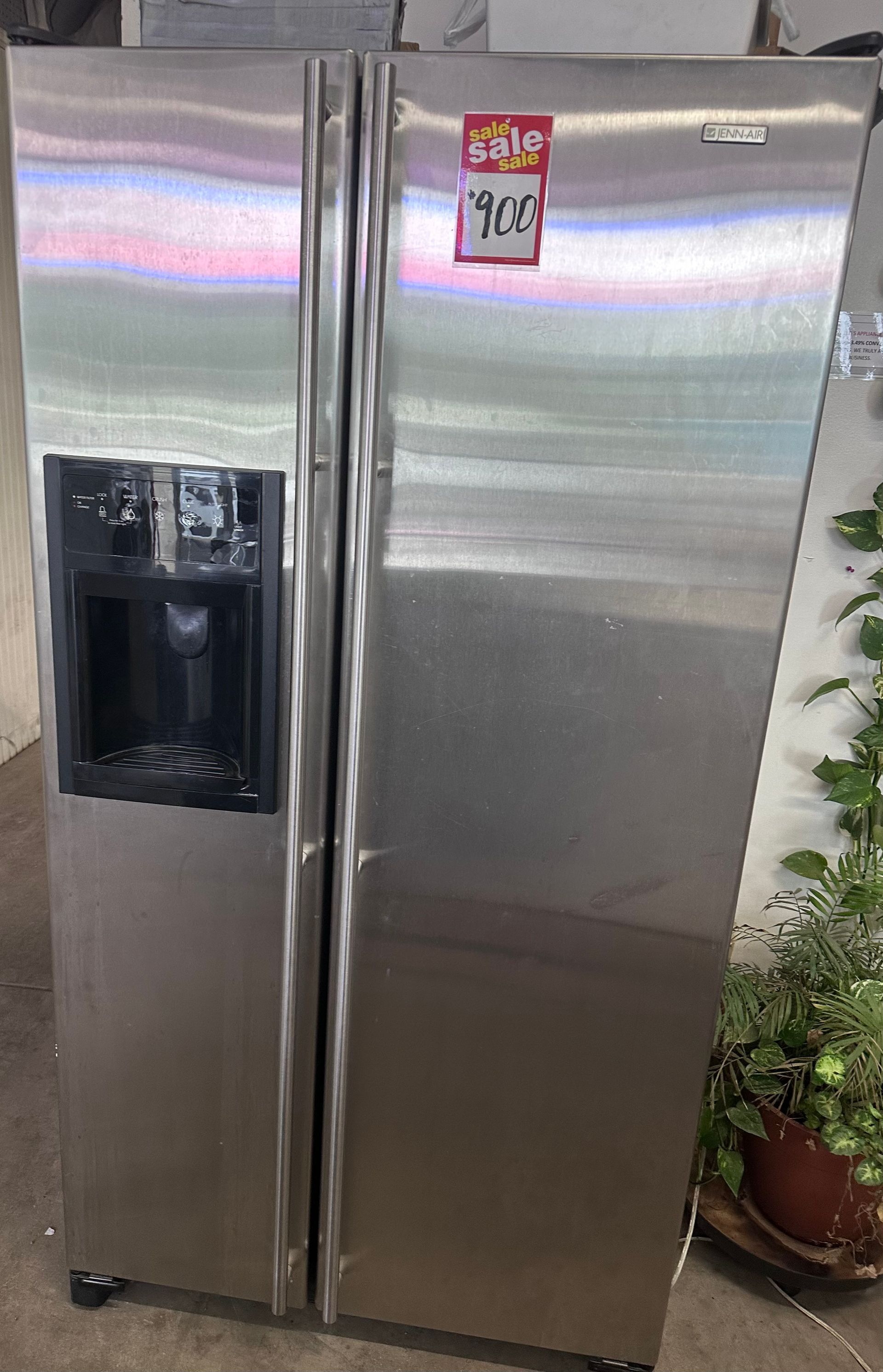 A stainless steel refrigerator with a water dispenser is sitting on a counter next to a potted plant.
