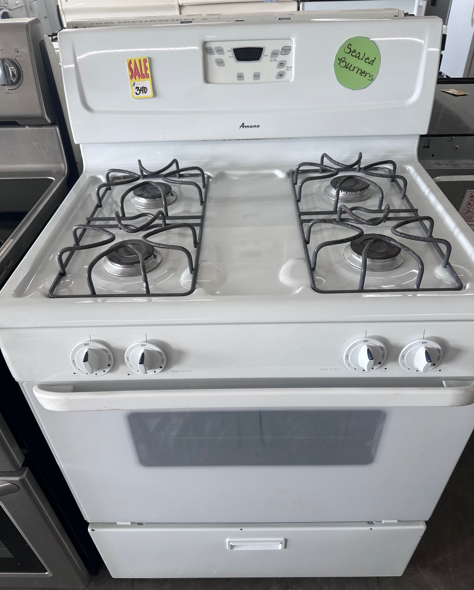 White gas range with four burners, oven, and storage drawer.