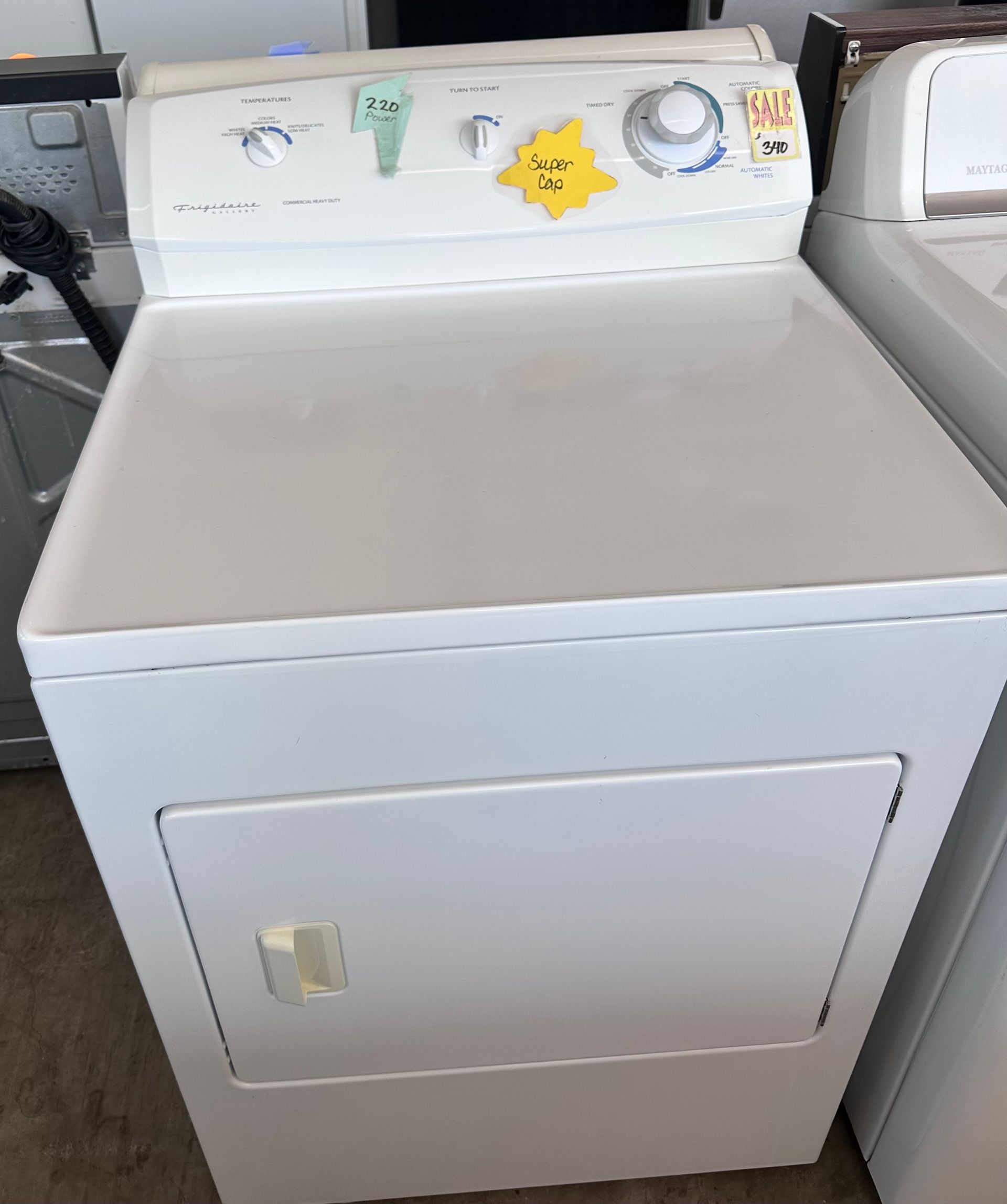 White Amana dryer with top controls and a front door, in a store setting.