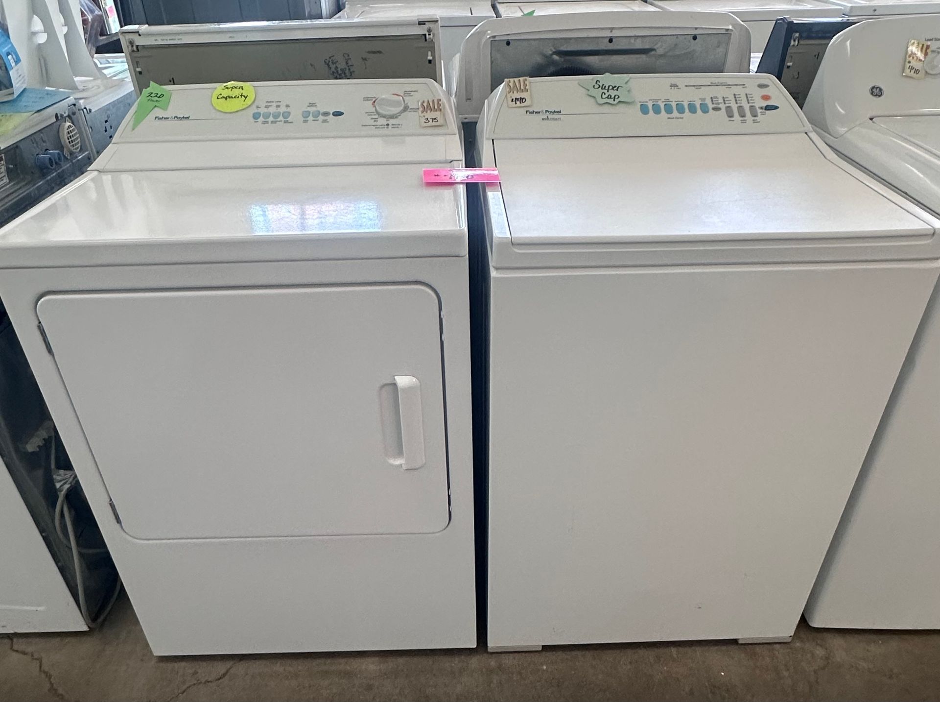Two white laundry machines side by side in a store aisle, with a dryer on the left and washer on the right.