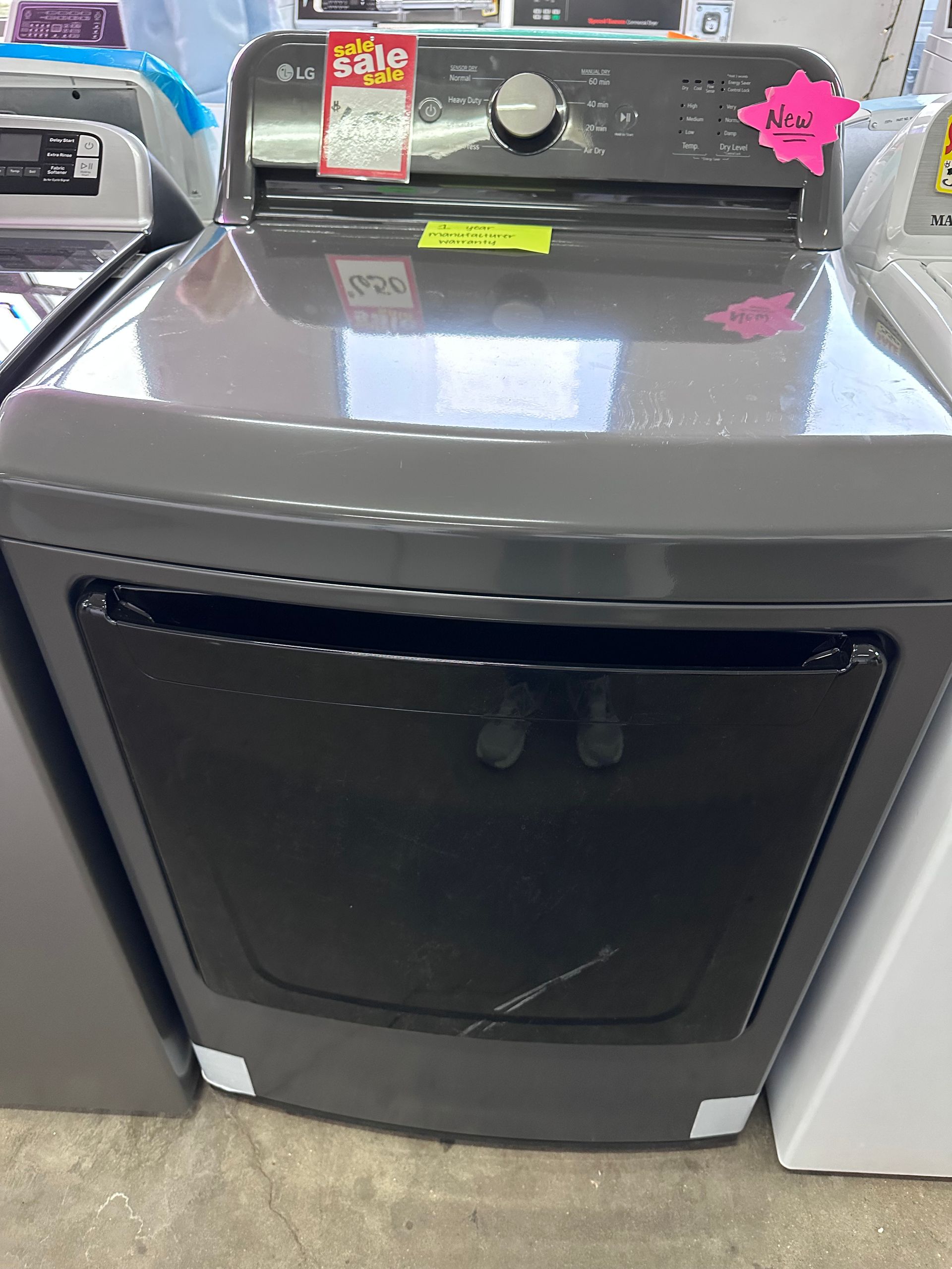 A gray clothes dryer with a black glass front door and control panel, displayed on a store showroom floor.