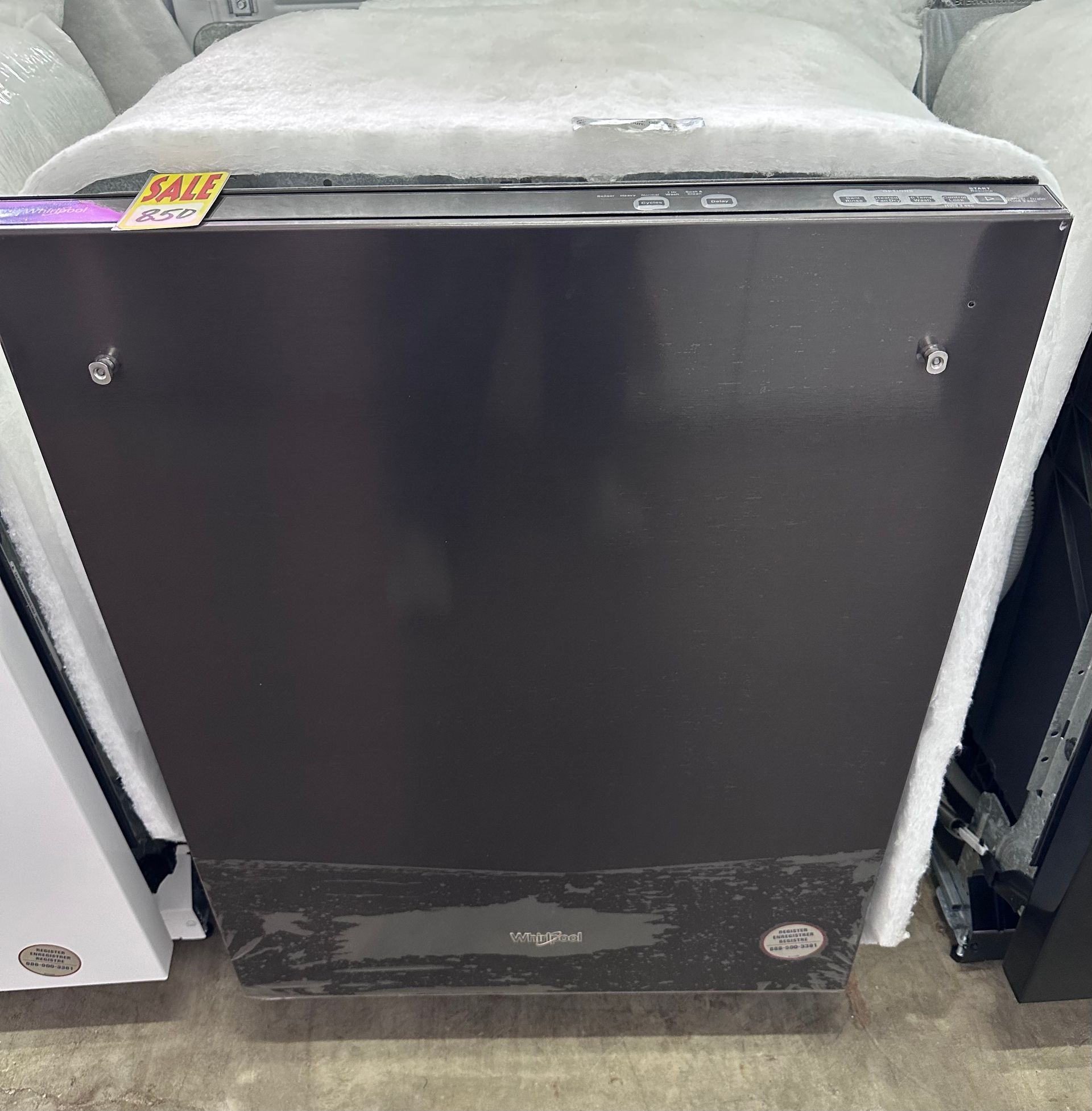 A black dishwasher with a protective foam covering on top, sitting in a retail store with a sale tag on the corner.