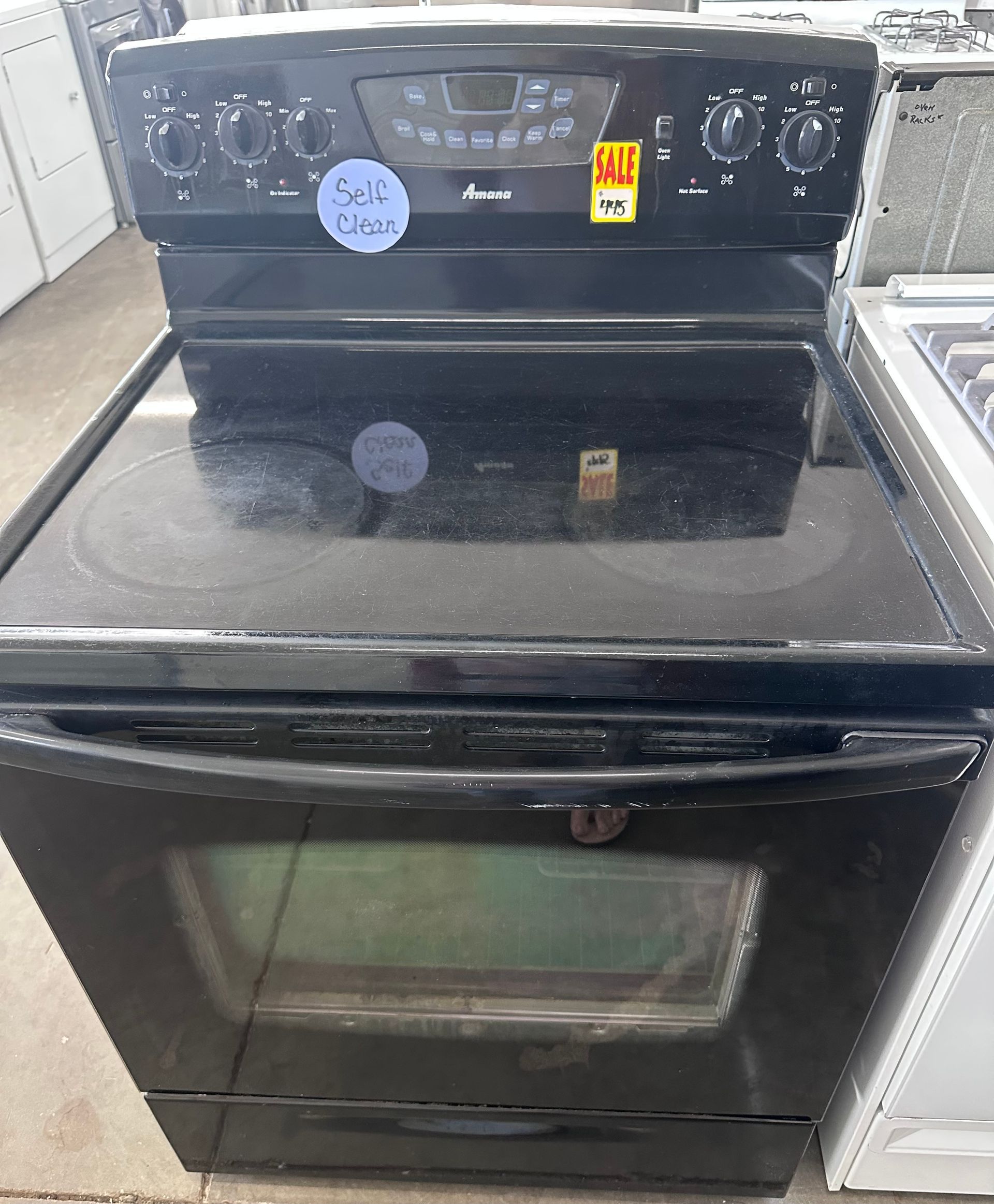 Black electric range with glass cooktop, oven below, knobs on top, and sale stickers.