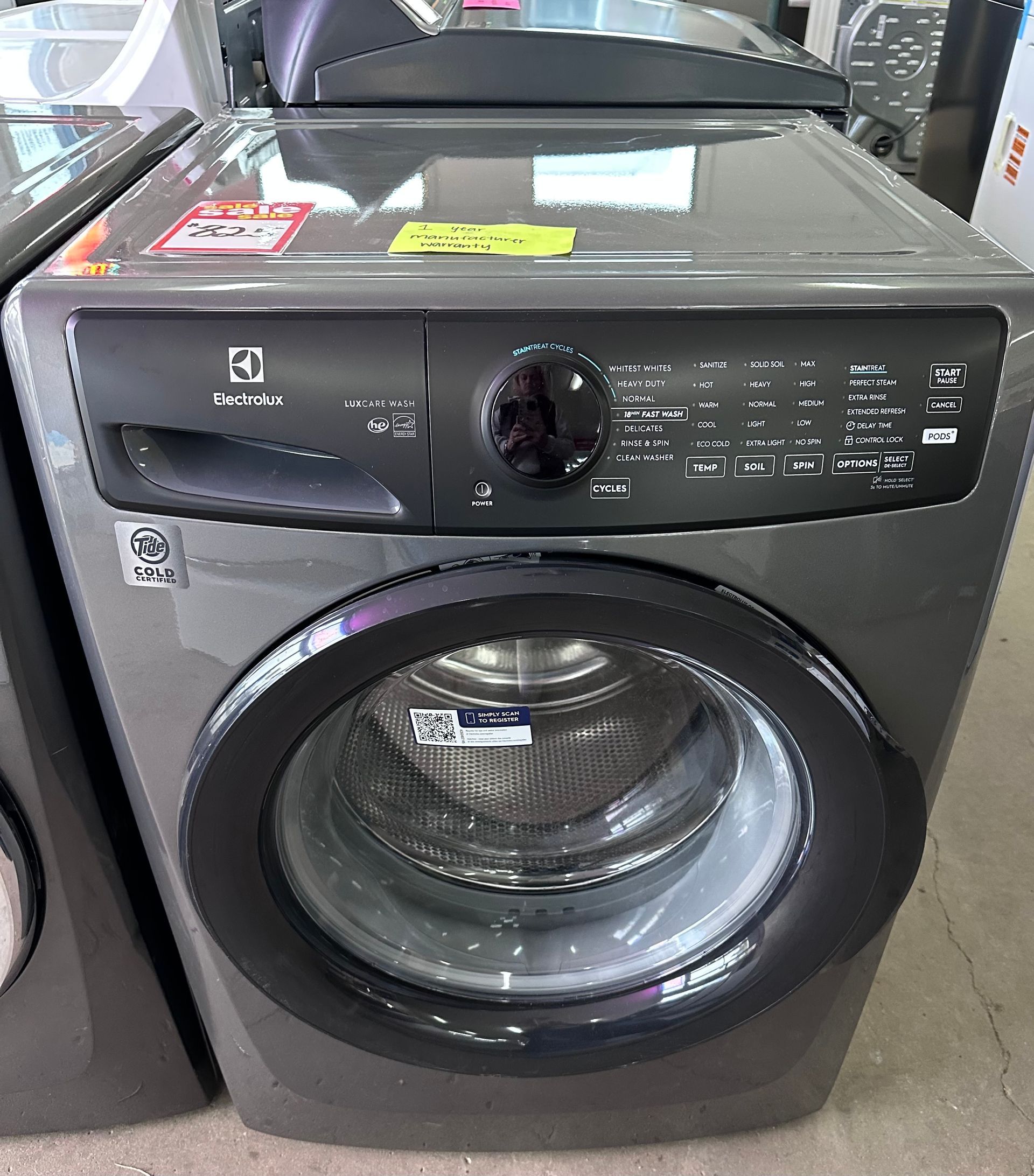 A gray front-load Electrolux washing machine with a black circular control panel and door, viewed in a retail setting.